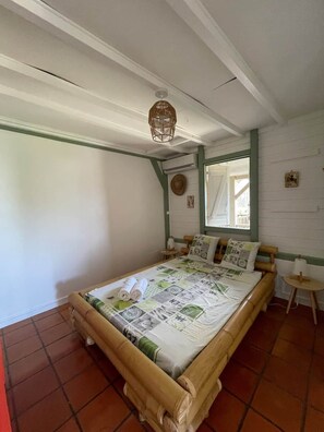 Une piĂšce comprenant un lit, une petite table, un luminaire suspendu et une fenĂȘtre.