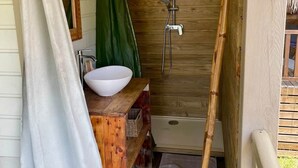 Ett badrum i en stuga med träpanel, en träbänk, ett vitt handfat, en dusch och en grön gardin.