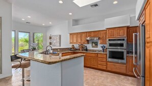Een moderne keuken met granieten aanrechtbladen, houten kastjes en roestvrijstalen apparatuur, plus een groot eiland.