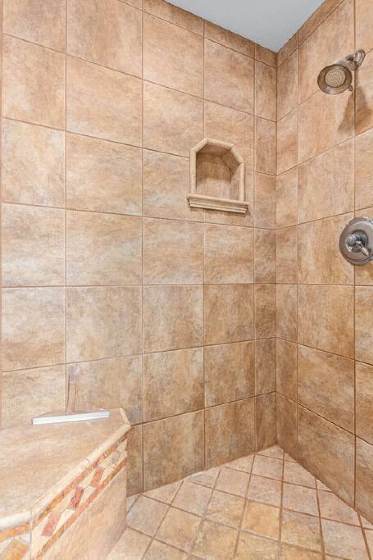 A shower area with beige tiles, a corner sink, and a showerhead.