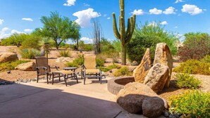 Een terras met stoelen en een tafel, omringd door rotsen en cactussen.