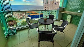 Un balcon avec vue sur l’océan, une table ronde avec des chaises et une petite plante en pot.