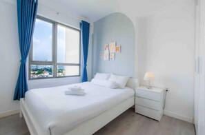 A bedroom with a large bed, a bedside table with a lamp, and a window with curtains.