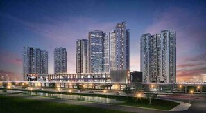 Een hoog uitgebouwd appartementencomplex met meerdere torens, een goed verlichte voetgangersbrug en een aangelegde zone met een waterpartij.