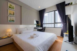 A hotel room with a large bed, a desk with a chair, a flat-screen TV, and a window with curtains.
