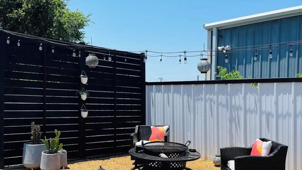 A backyard with a black fence, outdoor furniture, potted plants, and a fire pit. - Tiny home in Watauga. “Casita”  Beautiful Cottage! (Watauga)