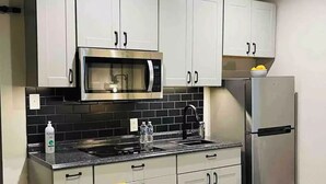 A modern kitchen with grey cabinets, a stainless steel refrigerator, a microwave, and a black tiled backsplash. - Tiny home in Watauga. “Casita”  Beautiful Cottage! (Watauga)