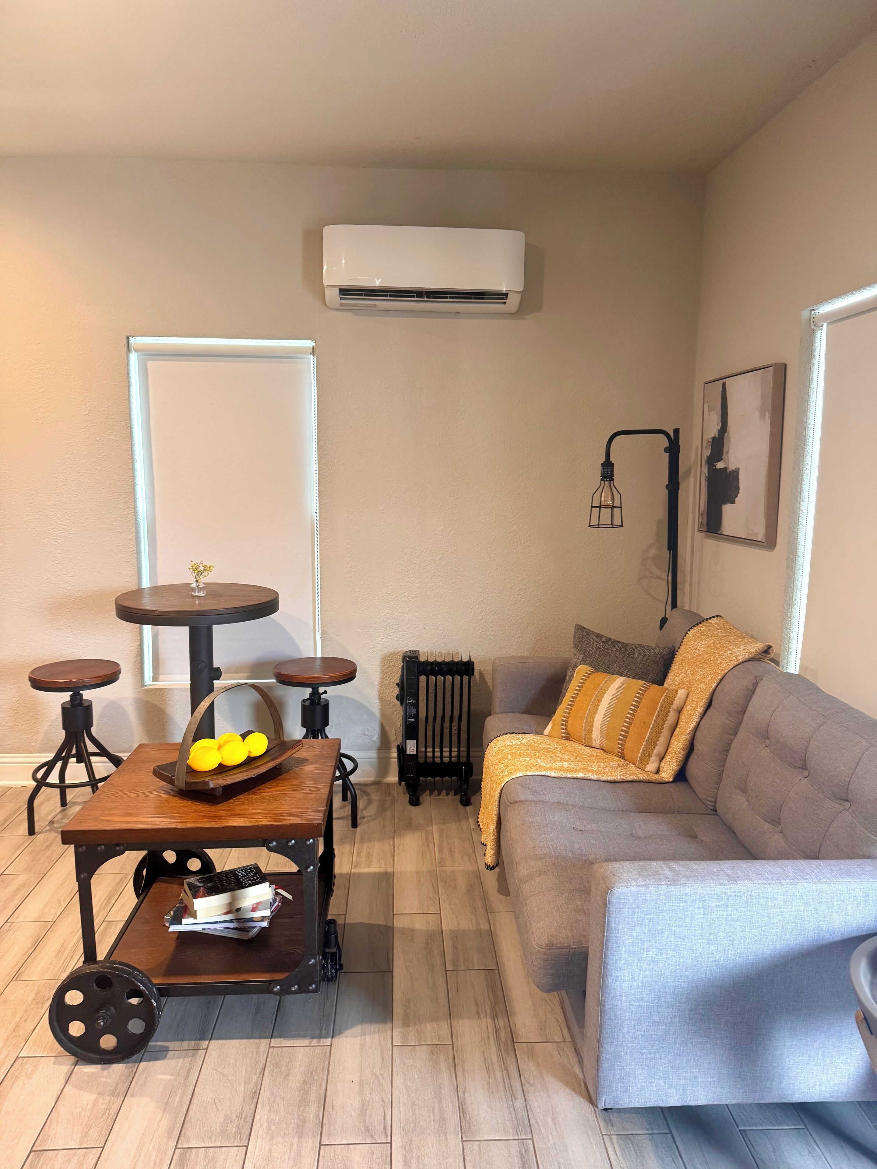 A cozy living room with a grey sofa, a small round table, a vintage cart, and a radiator.