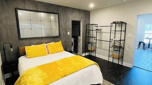 A modern bedroom with a large bed, a grey accent wall, and a view of the outside. - Tiny home in Watauga. “Casita”  Beautiful Cottage! (Watauga)