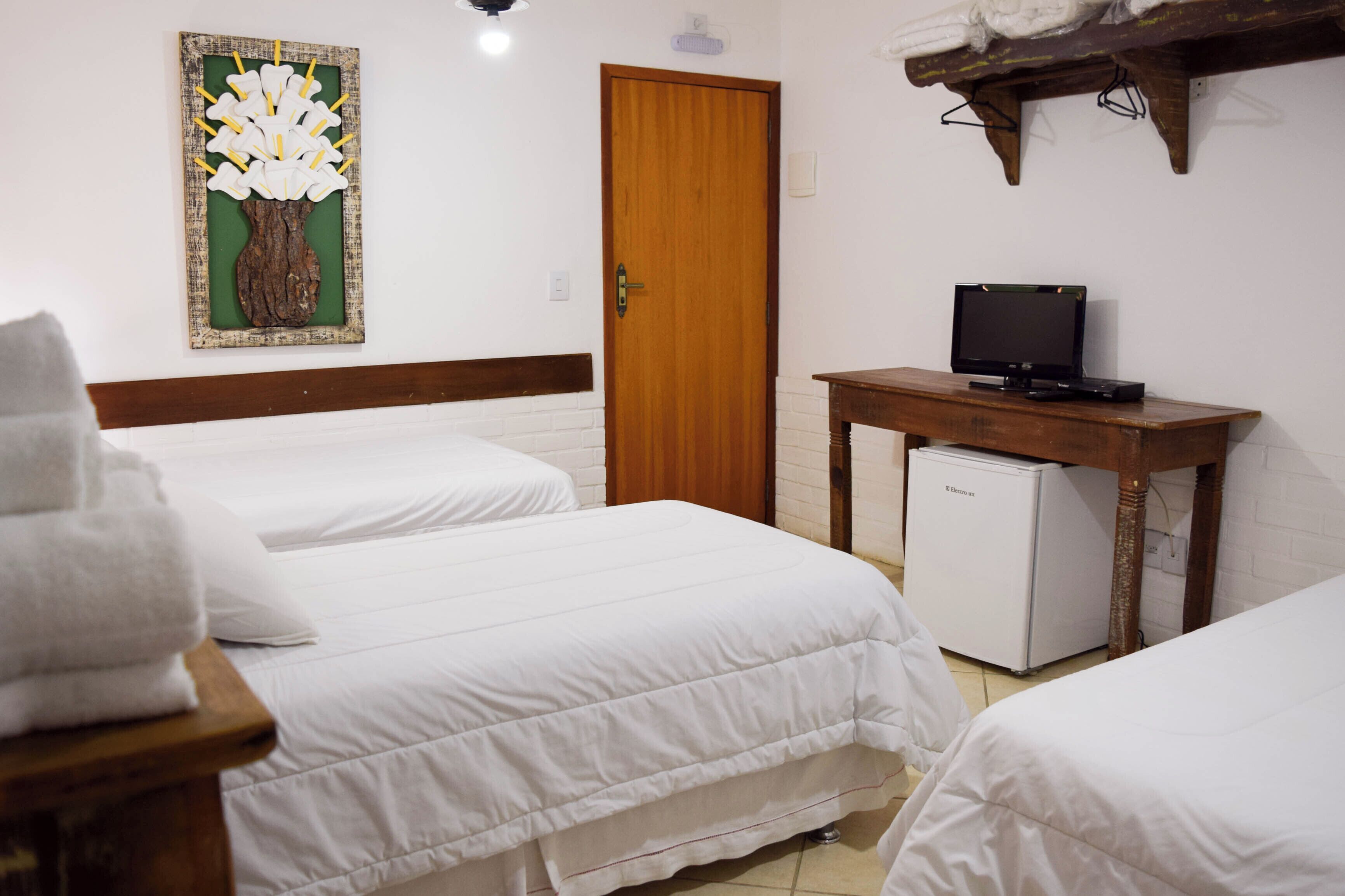 A hotel room with two beds, a small desk with a television, and a refrigerator.