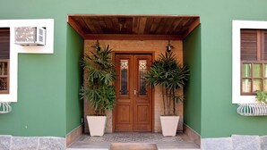 Una entrada de edificio con puerta de madera, dos plantas en macetas y suelo de baldosas.
