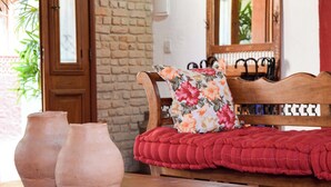 Un banco de madera con un cojín floral y una cubierta acolchada roja, una pared de ladrillo y una puerta de madera.