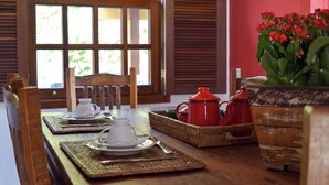 Un comedor con una mesa de madera preparada para el té, una cesta de mimbre y una olla roja.