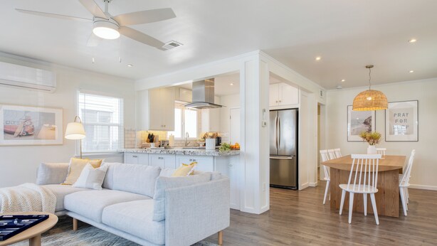 Una cocina moderna con armarios blancos, un refrigerador de acero inoxidable y una zona de comedor con una mesa de madera y sillas blancas.