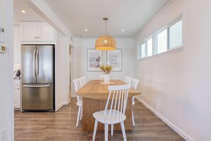 A modern kitchen with a stainless steel refrigerator, a wooden dining table with white chairs, and a pendant light. - Surfrider I by AvantStay | Walk to the Beach + Patio (Newport Beach)