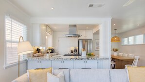 Una cocina moderna con armarios blancos, un refrigerador de acero inoxidable y un comedor con mesa y sillas de madera.