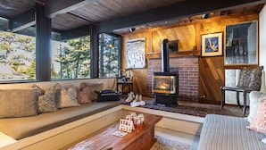 A cozy living room with a fireplace, wooden beams, a sofa with patterned cushions, and a coffee table with jars.