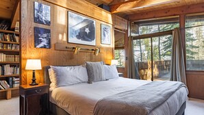 A wooden cabin bedroom with a large bed, bookshelves, and framed pictures on the walls.