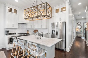 A modern kitchen with white cabinetry, a central island with bar stools, stainless steel appliances, and a geometric pendant light.