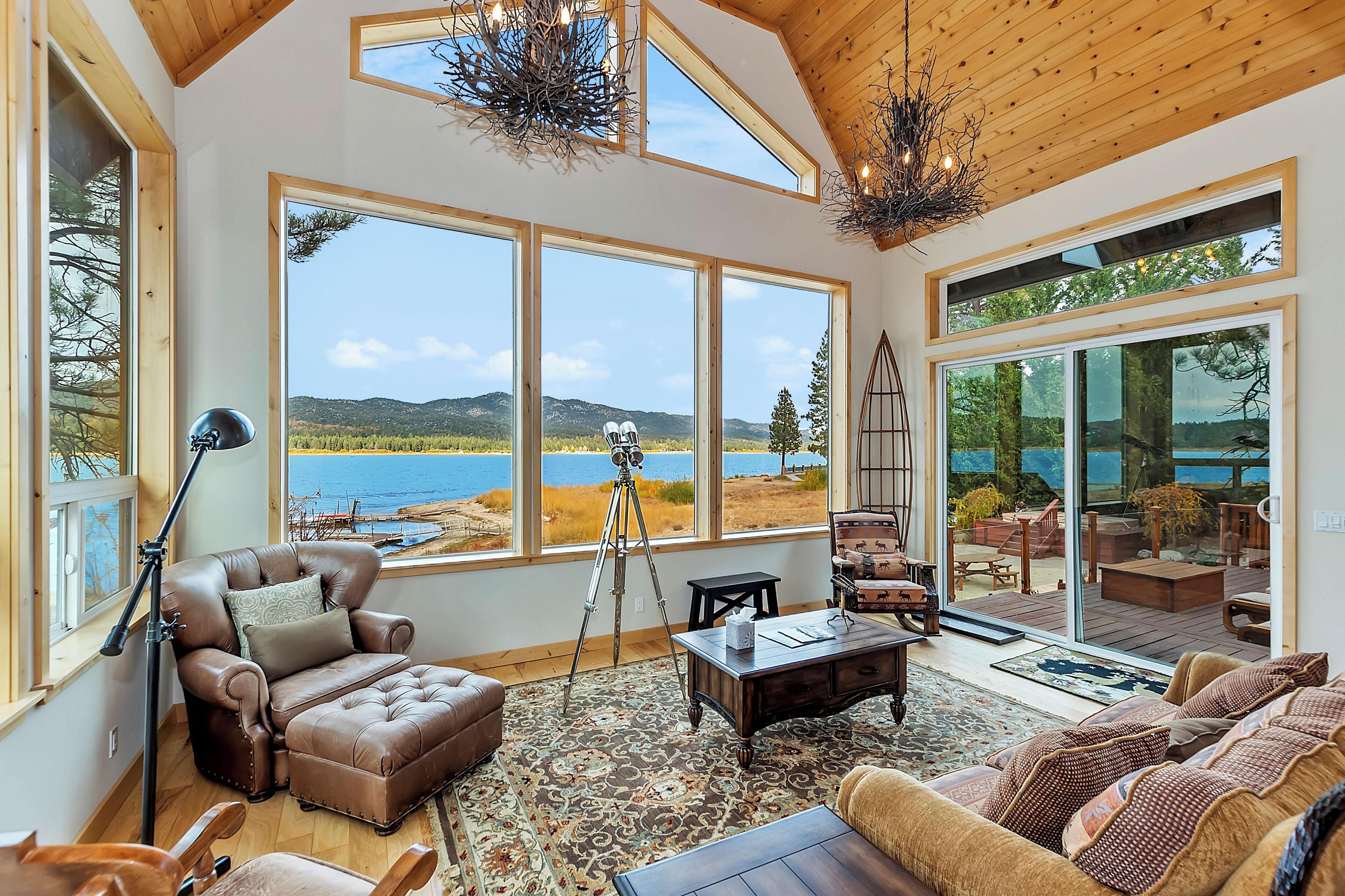 A spacious living room with large windows, a leather sofa, a coffee table, and a view of a lake and mountains.