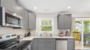 A modern kitchen with grey cabinets, a stainless steel microwave, a built-in oven, a sink, and a dishwasher. - Magnolia Sycamore by AvantStay | Near Downtown, Biltmore Estate, Hiking Trails (Asheville)