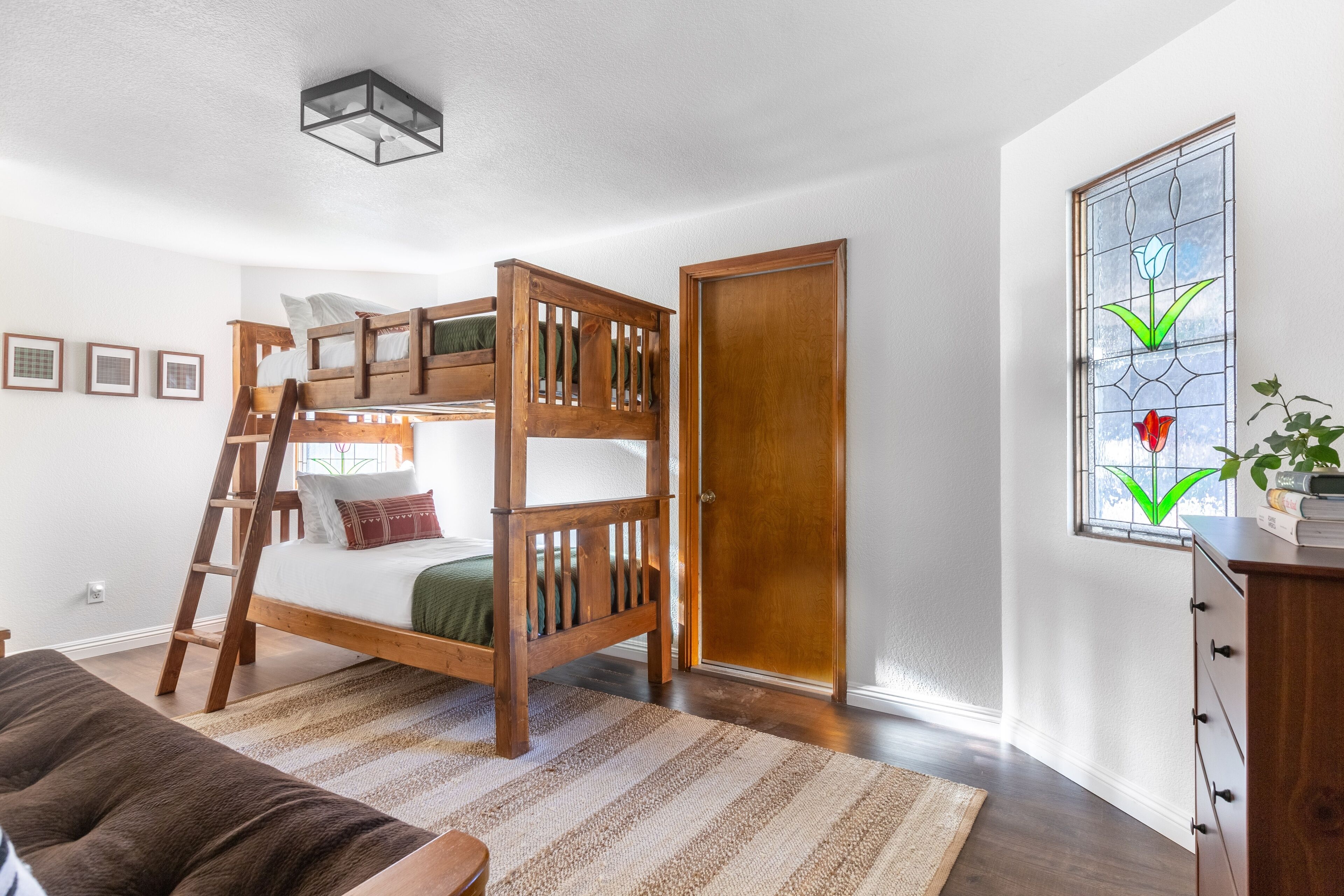 Habitación con literas, una escalera de madera, un escritorio pequeño y una ventana con un diseño de vidrio de colores.