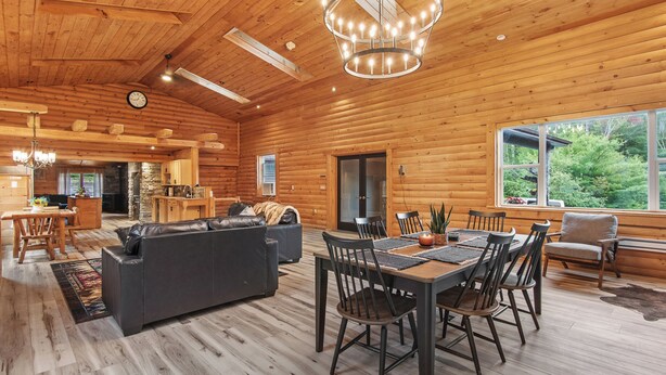 Ruim houten blokkenhut interieur met een eethoek, een woonkamer met een bank, en een keuken op de achtergrond.