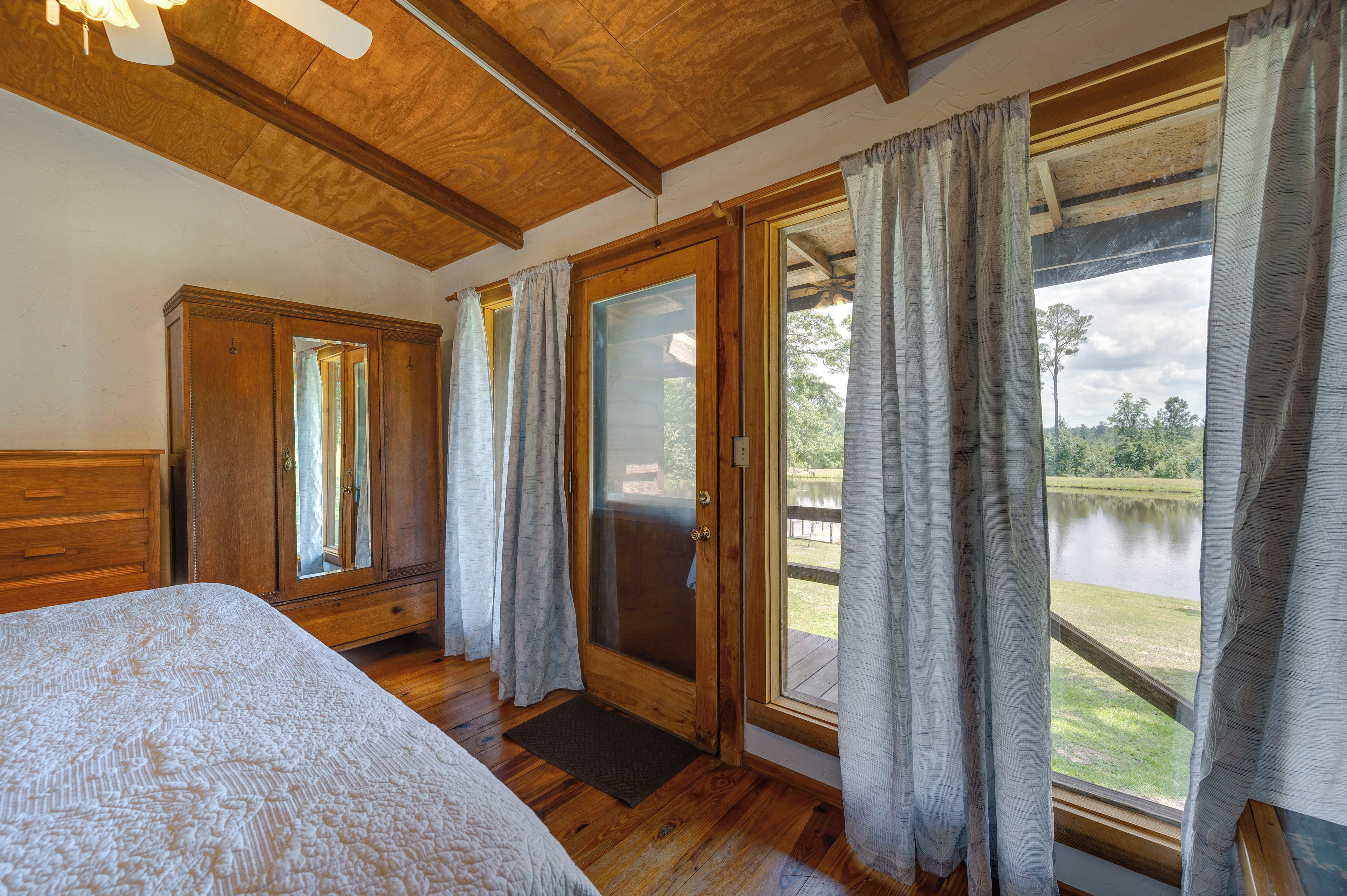 Camera da letto con soffitto in legno, un letto grande, un armadio in legno e una porta scorrevole in vetro che dà su un balcone con vista su un lago.