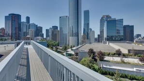 Un horizonte urbano con modernos rascacielos, un puente peatonal y algo de vegetación.