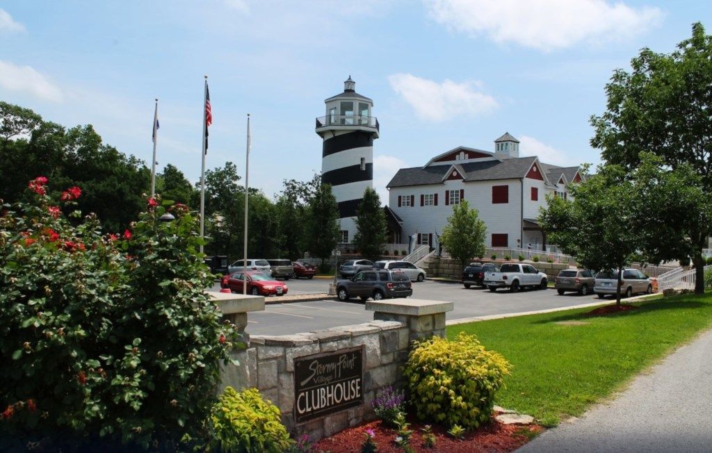 A clubhouse with a lighthouse, a parking lot, and a sign indicating the name.