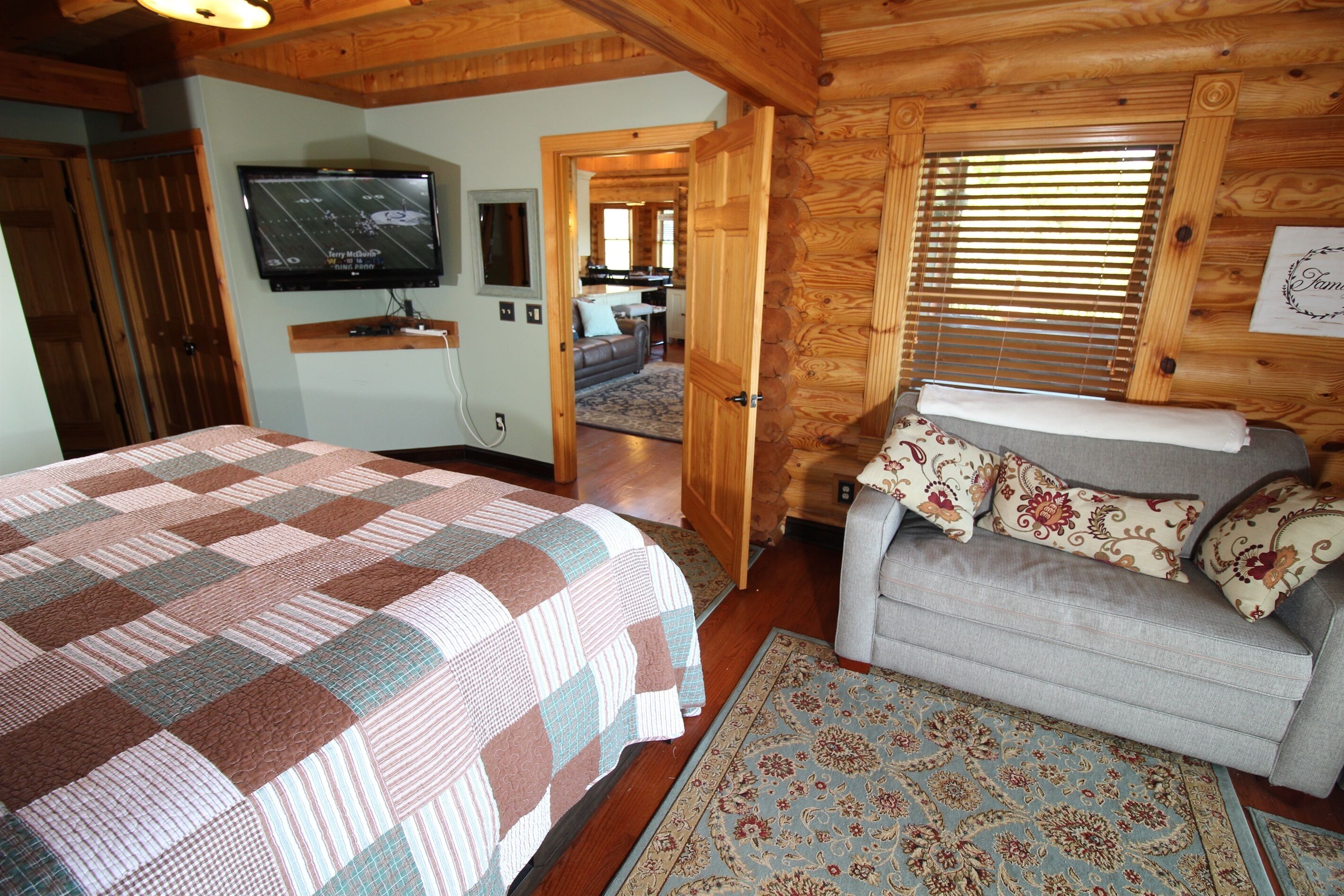 Une chambre confortable aménagée dans un chalet en bois, avec un grand lit, un canapé et un téléviseur fixé au mur.