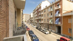 A residential street with multi-story buildings, parked cars, and balconies.