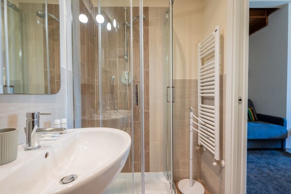 A bathroom with a white sink, a glass-enclosed shower, and a white radiator.