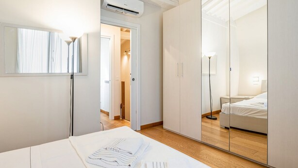 A hotel room with a bed, a mirror, a wardrobe, and an air conditioning unit. - GuestHost - Cozy and modern 65 sqmapartment, on two levels, able to accommodate up to 6 people, located on the ground floor of a building (a few steps to access). The property is located in a quiet area, about 500 meters from Piazza della Libertà, and w (Firenze)