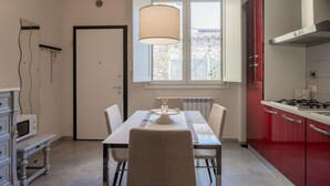 A dining area with a table, chairs, a hanging light fixture, a red kitchen, and a door. - GuestHost - Cozy and modern 65 sqmapartment, on two levels, able to accommodate up to 6 people, located on the ground floor of a building (a few steps to access). The property is located in a quiet area, about 500 meters from Piazza della Libertà, and w (Firenze)
