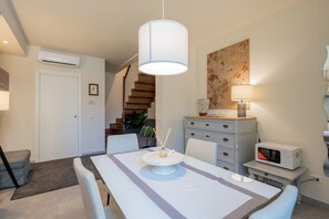 Un espace repas comprenant une table, des chaises, un luminaire suspendu, un four à micro-ondes et un escalier.