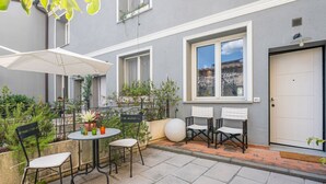 A courtyard with a table and chairs, potted plants, and a white door. - GuestHost - Cozy and modern 65 sqmapartment, on two levels, able to accommodate up to 6 people, located on the ground floor of a building (a few steps to access). The property is located in a quiet area, about 500 meters from Piazza della Libertà, and w (Firenze)