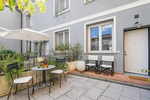 Une cour avec une table et des chaises, des plantes en pot et une porte blanche.