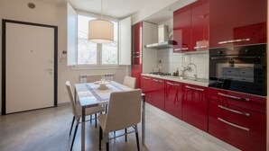 A modern kitchen with red cabinets, a dining table with chairs, a window with natural light, and a white door. - GuestHost - Cozy and modern 65 sqmapartment, on two levels, able to accommodate up to 6 people, located on the ground floor of a building (a few steps to access). The property is located in a quiet area, about 500 meters from Piazza della Libertà, and w (Firenze)