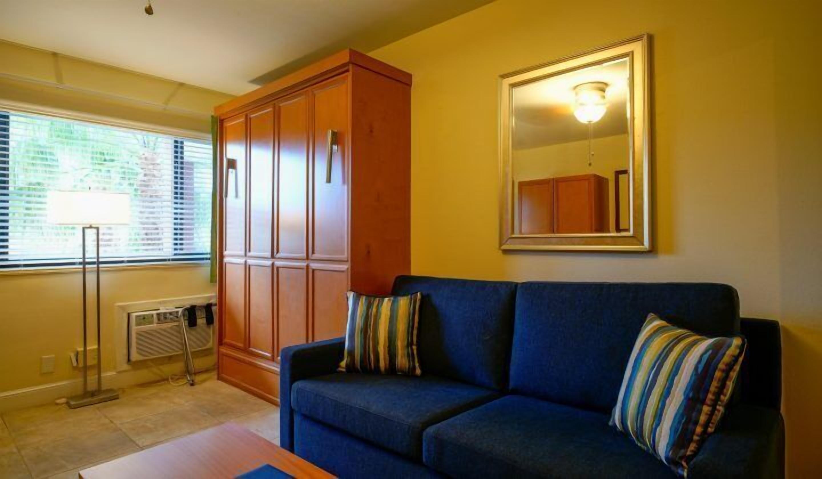 A living room with a blue sofa, a wooden cabinet, a mirror, and a radiator.