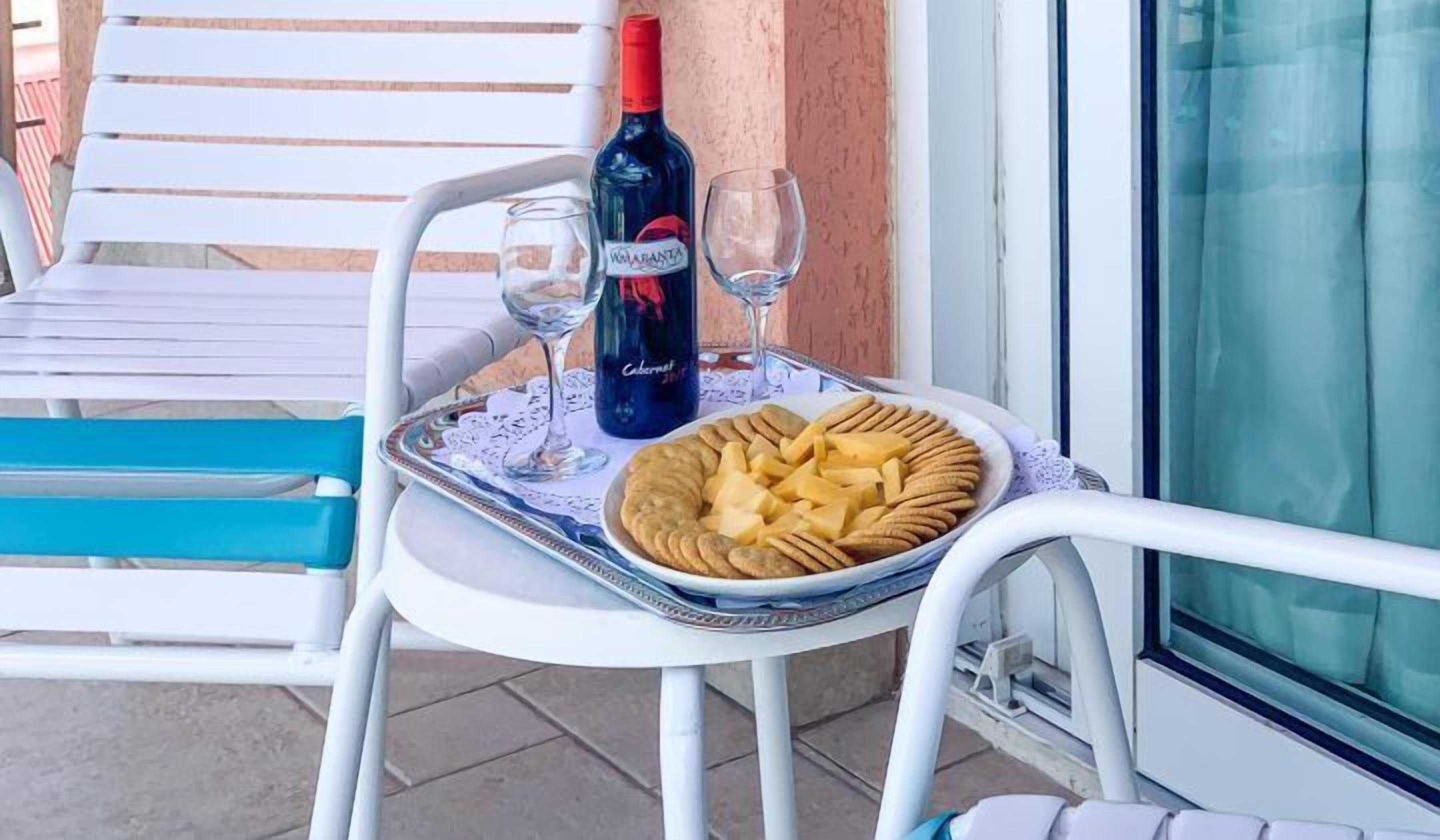 A table with a bottle of wine, two glasses, and a plate of snacks on a balcony.