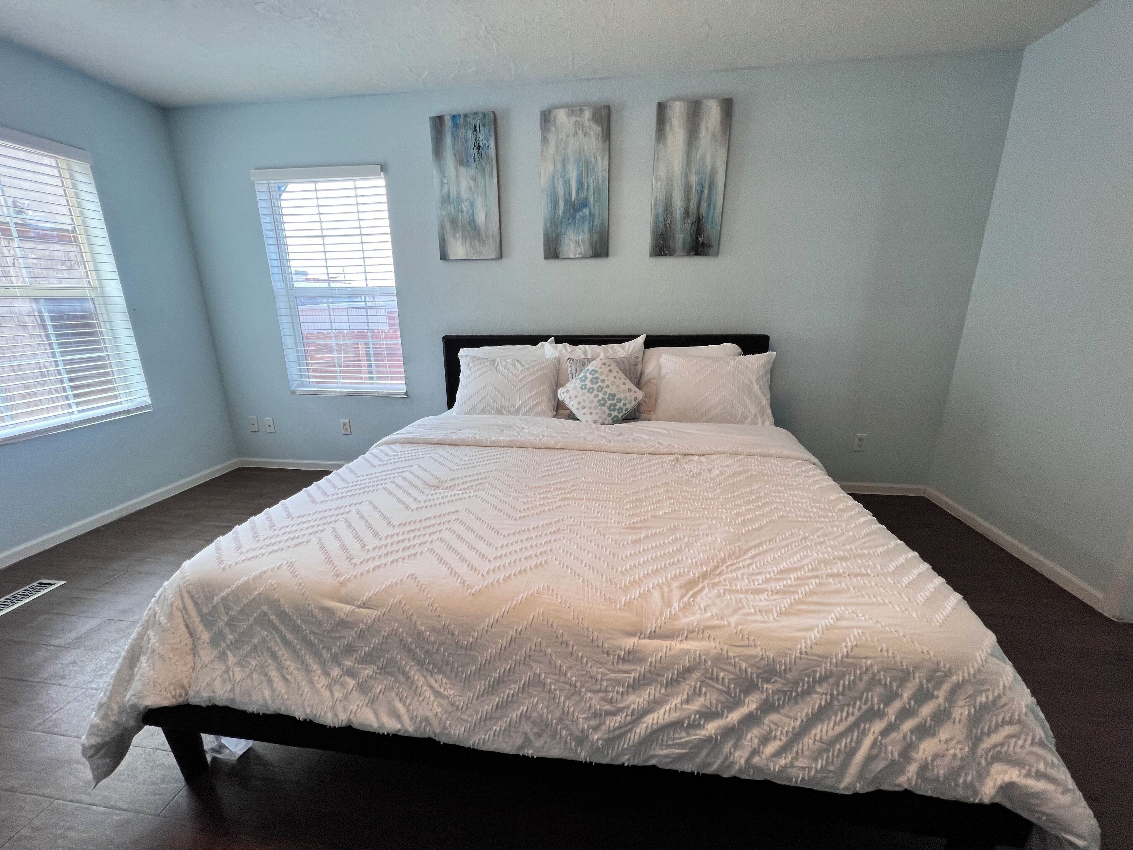 A bedroom with a large bed, light blue walls, and three abstract paintings above the bed.