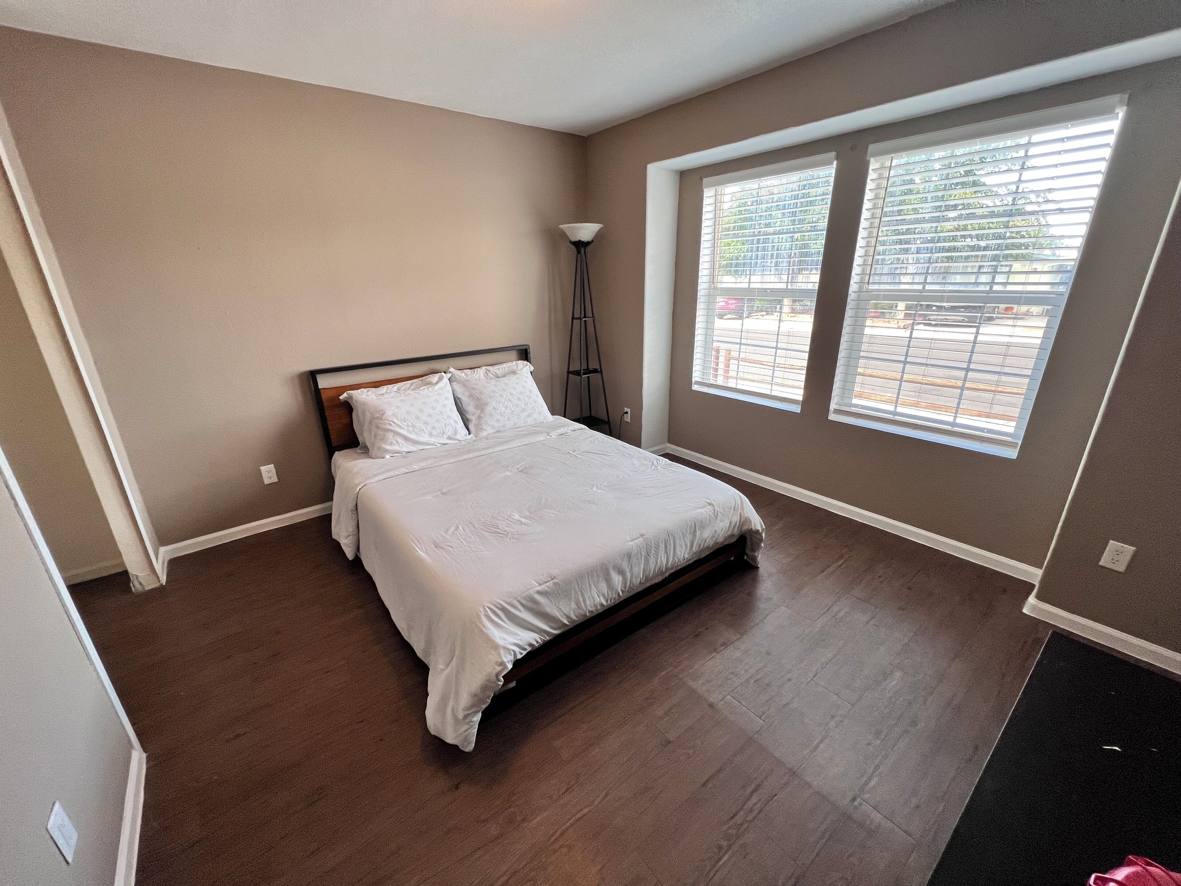 Une chambre à coucher avec un lit, une lampe sur pied et une grande fenêtre équipée de stores.