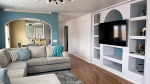 Ein modernes Wohnzimmer mit Ecksofa, einem Flachbildfernseher an einer weißen Regaleinheit und einem Deckenventilator.