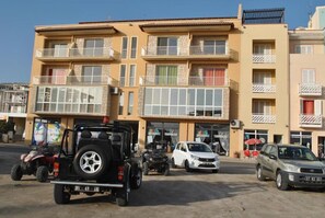 Un immeuble à plusieurs étages doté de balcons, un jeep garé et une voiture blanche devant.