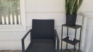 Une chaise en osier noir avec une structure en métal, un pot contenant une plante serpent et une étagère en métal sur laquelle est apposée une pancarte « Il est interdit de fumer ».