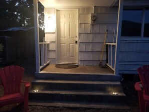 Une entrée de maison avec une porte blanche, des marches menant au porche et une chaise rouge sur la gauche.