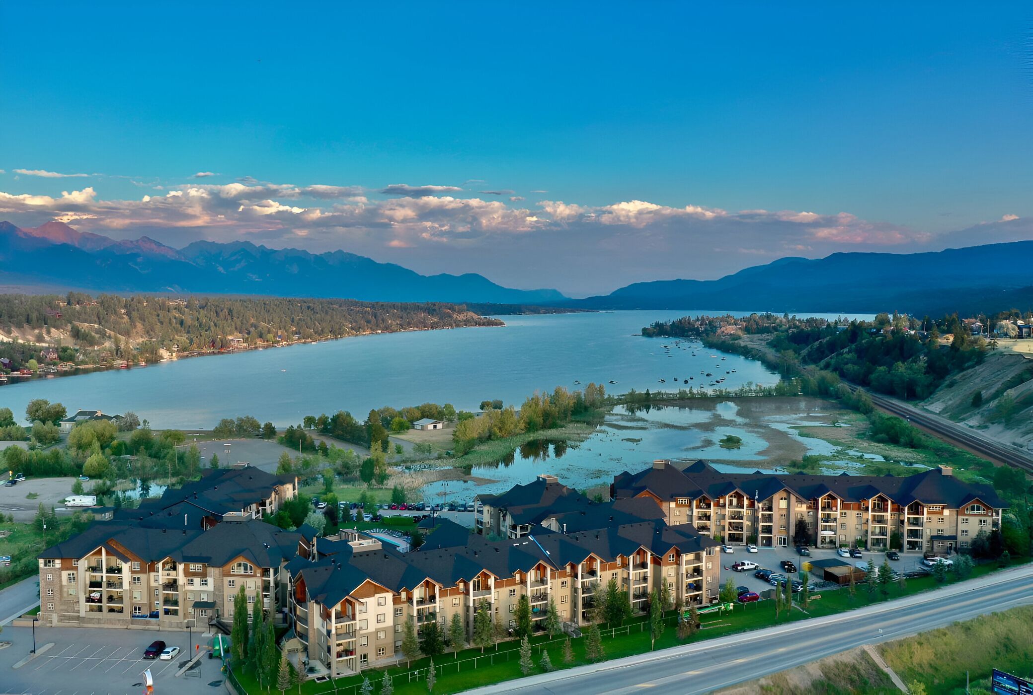 Un hôtel à plusieurs étages doté d’un parking, situé près d’un lac, avec des montagnes en toile de fond.