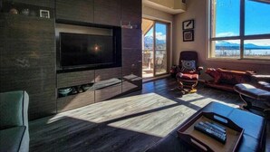 Ein modernes Wohnzimmer mit einem großen Flachbildfernseher, dunklem Holzboden und Bergblick durch große Fenster.