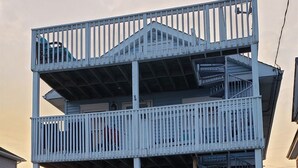 A multi-story building with a balcony on the second floor, a porch with mailboxes, and a small garden area with a basket of flowers. - A Sandcrab & Jellyfish Walk Into a Sand-Bar (Ocean City)